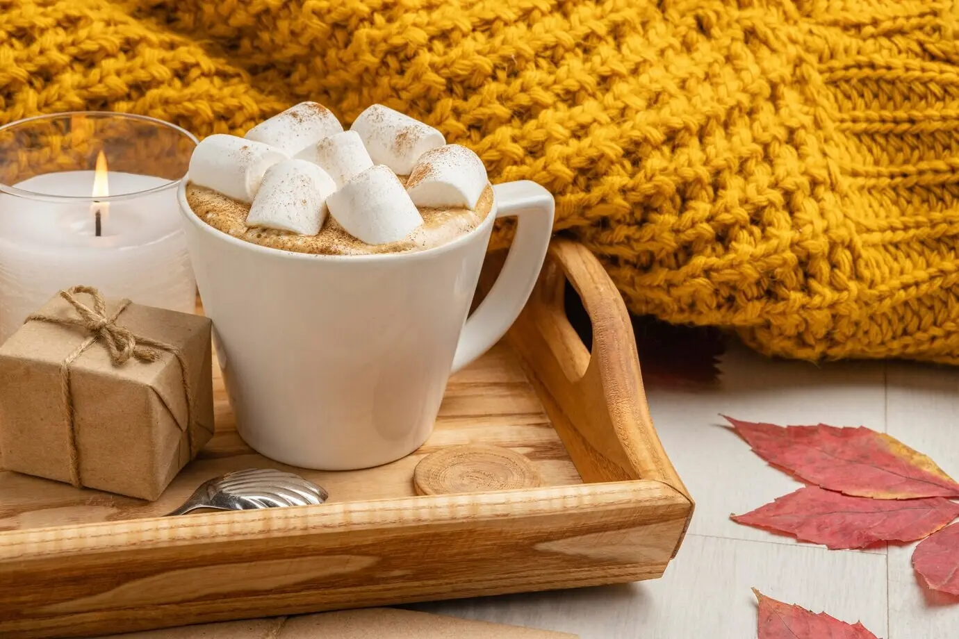 Tasse mit Marshmallows, Geschenk und Kerze neben einem Pullover.